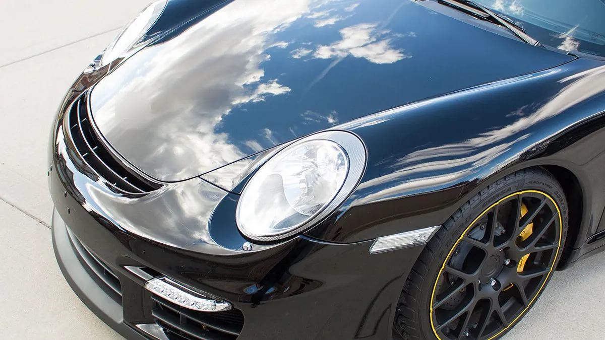 Cofre negro de un Porsche con reflejo de nubes tras corregir la pintura