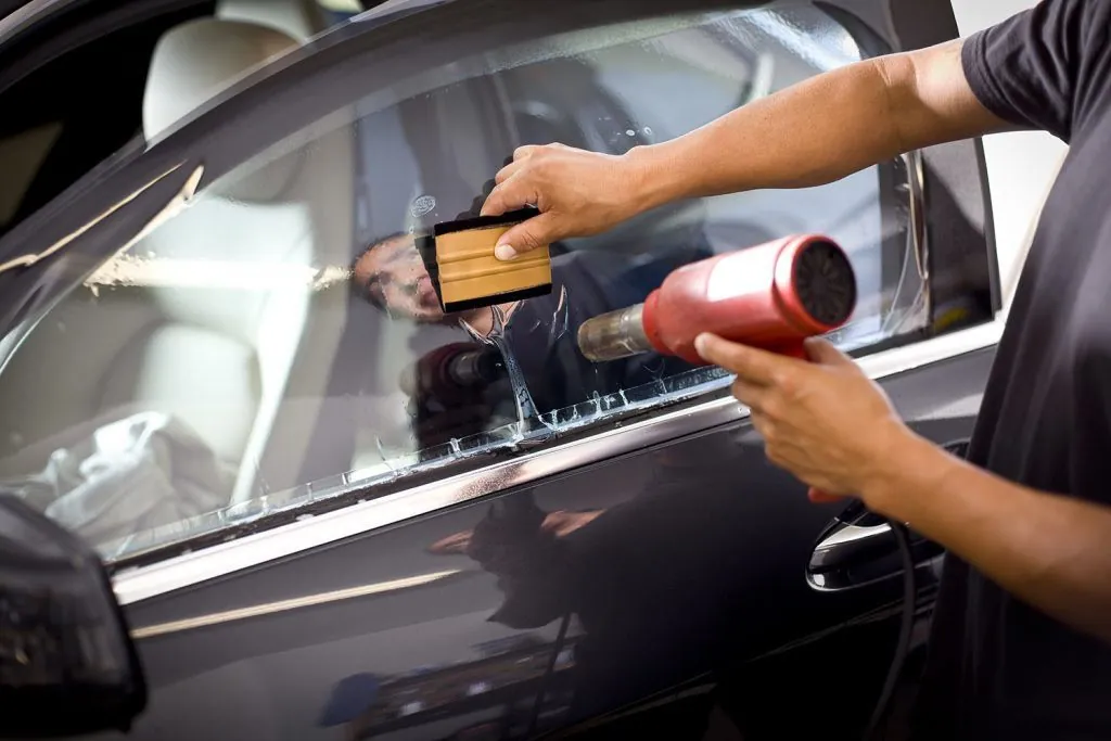 Pistola de calor y espátula dorada sobre la ventana de un auto