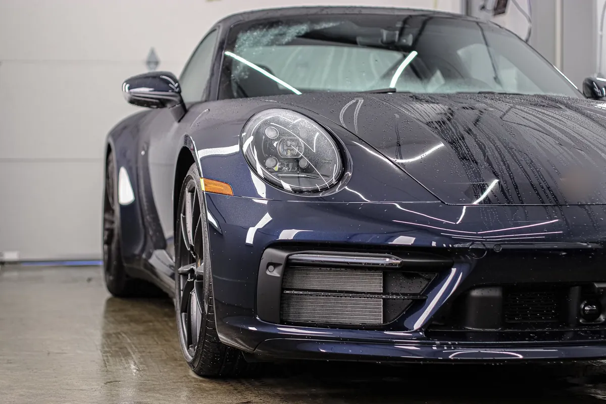 Porsche azul oscuro en bahía de lavado con faro limpio