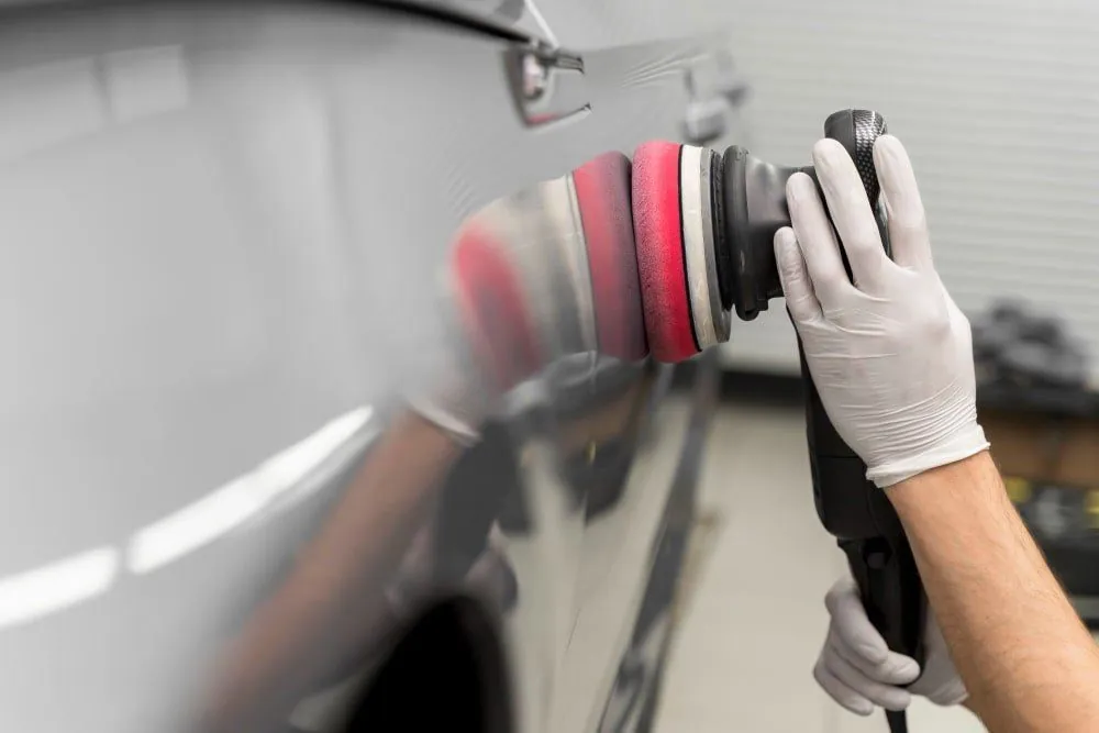 Pulidora orbital con pad rojo sobre el costado gris de un auto